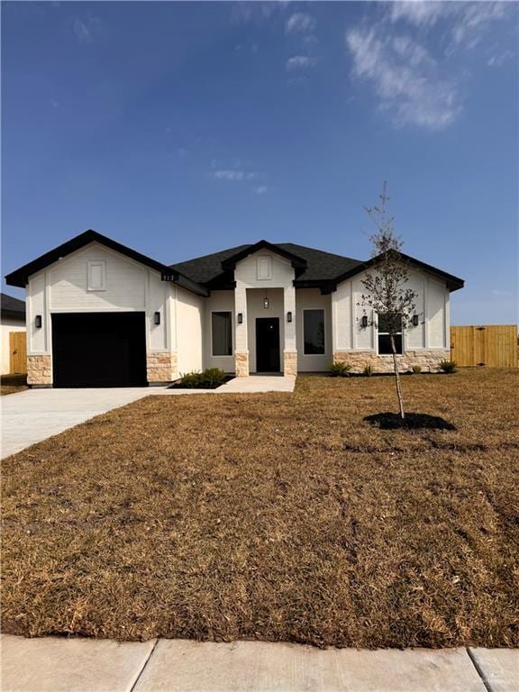 view of front of house with a garage, driveway, stone siding, fence, and a front lawn