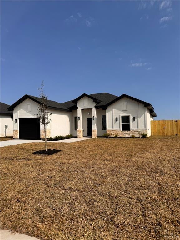 view of front of home with an attached garage, fence, stone siding, driveway, and a front lawn