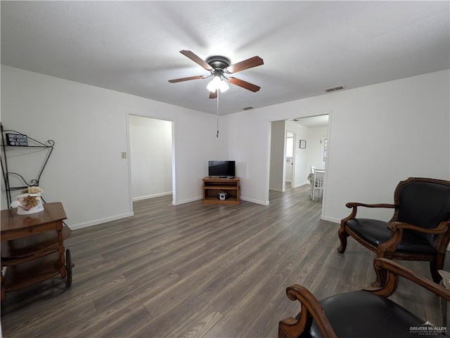 living area with dark wood-type flooring, ceiling fan, and a textured ceiling