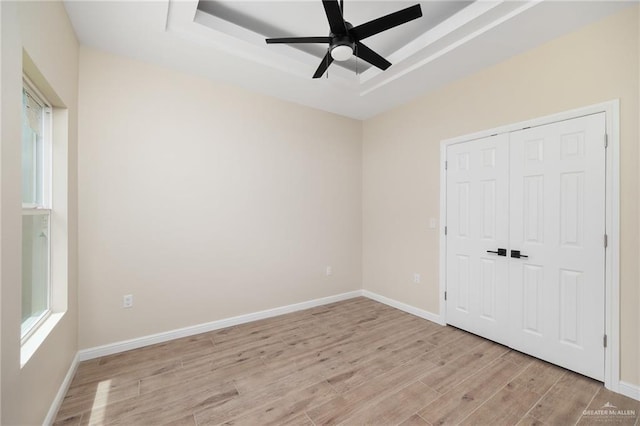 unfurnished bedroom with a raised ceiling, ceiling fan, a closet, and light wood-type flooring