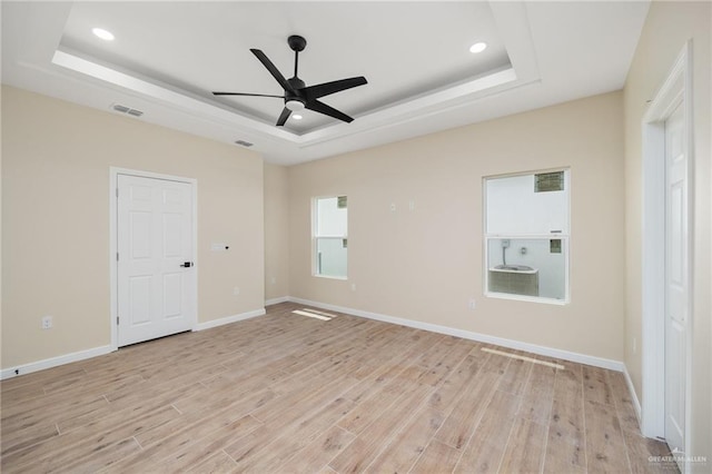 empty room featuring a raised ceiling, ceiling fan, and light hardwood / wood-style floors