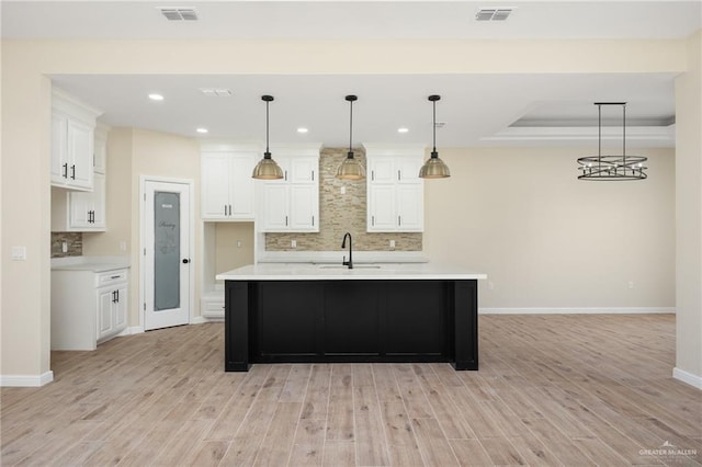 kitchen featuring white cabinets, an island with sink, pendant lighting, and light wood-type flooring