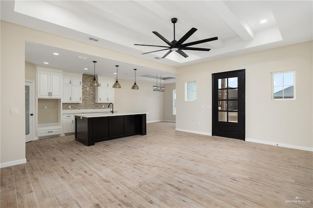 kitchen with sink, an island with sink, pendant lighting, white cabinets, and light wood-type flooring