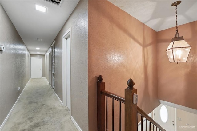 hall featuring visible vents, baseboards, an upstairs landing, a textured wall, and carpet