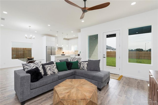 living room featuring ceiling fan with notable chandelier and light hardwood / wood-style floors