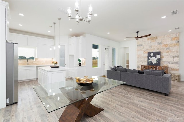 dining area with sink, ceiling fan with notable chandelier, and light hardwood / wood-style floors