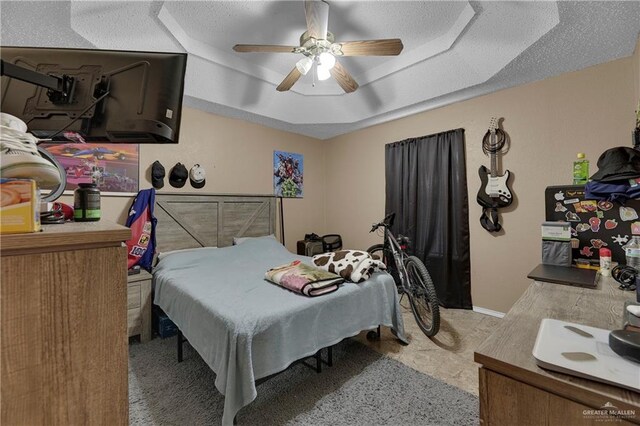 bedroom featuring a tray ceiling, ceiling fan, and a textured ceiling