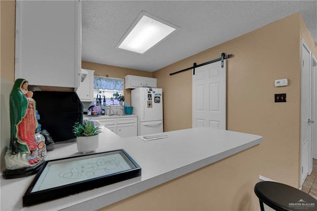 kitchen featuring kitchen peninsula, a textured ceiling, a barn door, white fridge, and white cabinetry