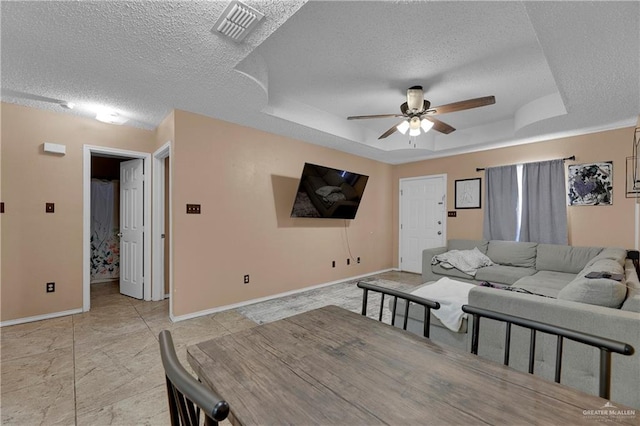 living room with a raised ceiling, ceiling fan, and a textured ceiling