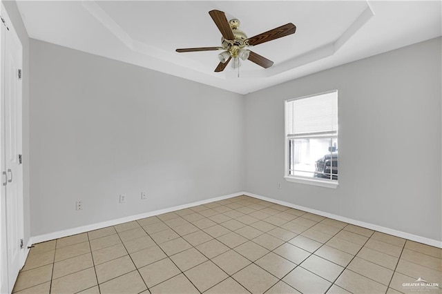 spare room with a tray ceiling, a ceiling fan, and baseboards