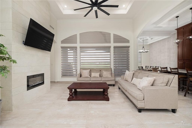 living room with ceiling fan with notable chandelier, a tray ceiling, and a tiled fireplace