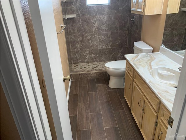 bathroom with a tile shower, vanity, and toilet