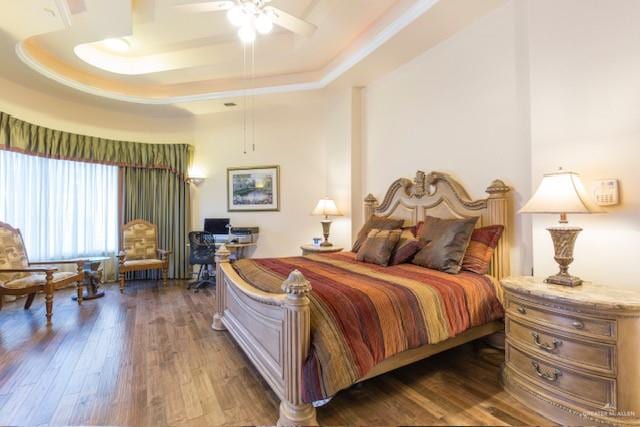 bedroom with dark hardwood / wood-style flooring, ceiling fan, and a raised ceiling