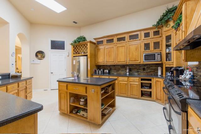 kitchen featuring a center island, wall chimney exhaust hood, light tile patterned floors, appliances with stainless steel finishes, and tasteful backsplash