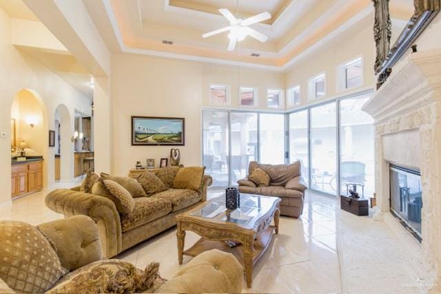 living room featuring a high ceiling, a tray ceiling, ceiling fan, and a premium fireplace