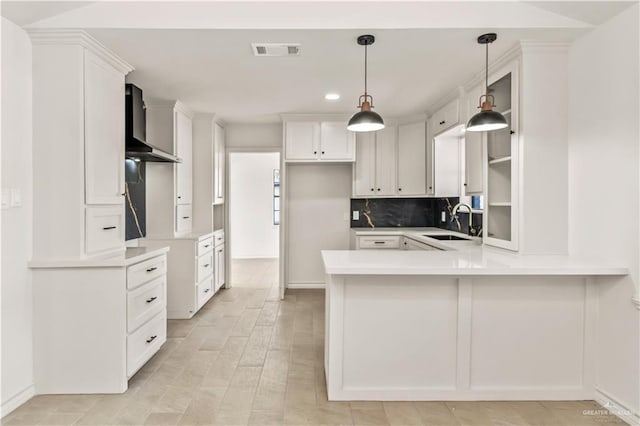 kitchen with sink, wall chimney exhaust hood, hanging light fixtures, kitchen peninsula, and white cabinets