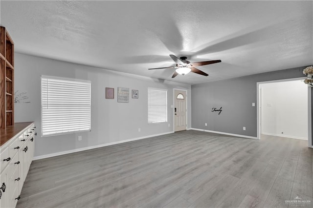 unfurnished living room featuring ceiling fan, a textured ceiling, and light wood-type flooring