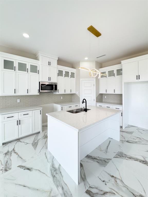 kitchen with sink, white cabinetry, pendant lighting, a kitchen island with sink, and decorative backsplash