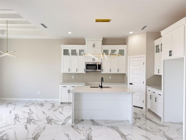 kitchen featuring white cabinetry, sink, decorative backsplash, hanging light fixtures, and a center island with sink