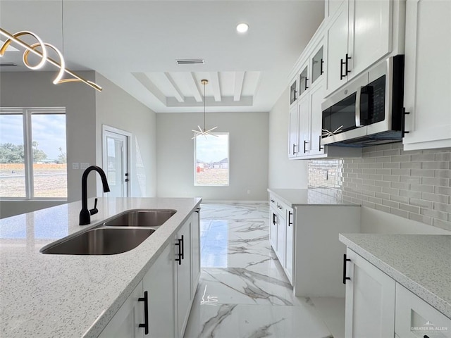 kitchen featuring hanging light fixtures, white cabinetry, sink, and a tray ceiling