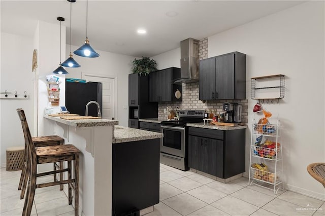 kitchen featuring stainless steel electric range oven, a kitchen breakfast bar, hanging light fixtures, wall chimney exhaust hood, and refrigerator