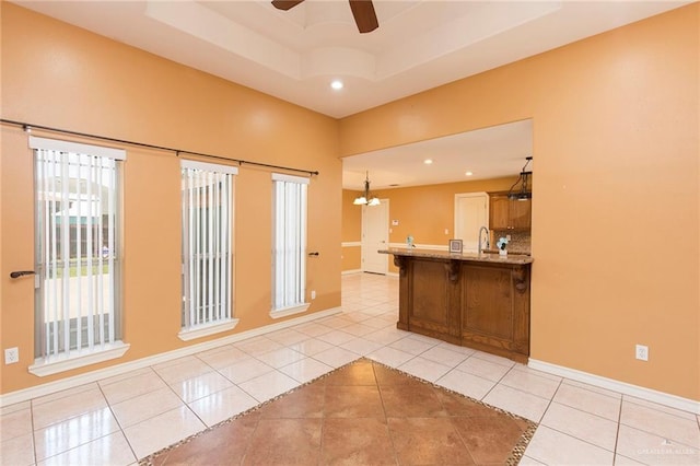 kitchen with a kitchen breakfast bar, ceiling fan with notable chandelier, a tray ceiling, sink, and light tile patterned flooring