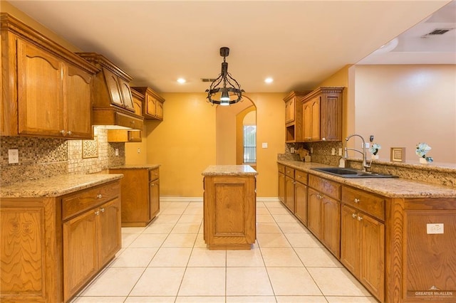 kitchen with light stone countertops, sink, light tile patterned floors, decorative light fixtures, and a kitchen island