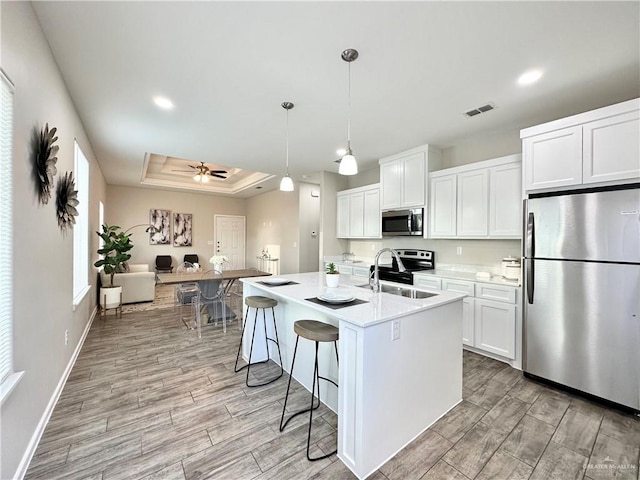 kitchen featuring sink, white cabinetry, hanging light fixtures, appliances with stainless steel finishes, and a kitchen island with sink