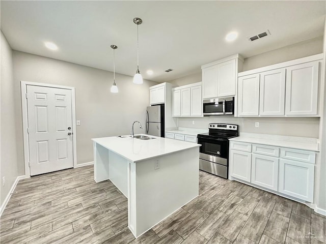 kitchen with sink, appliances with stainless steel finishes, a kitchen island with sink, white cabinets, and decorative light fixtures