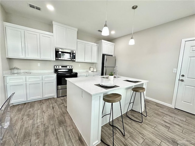 kitchen with white cabinetry, light stone counters, decorative light fixtures, a center island with sink, and appliances with stainless steel finishes