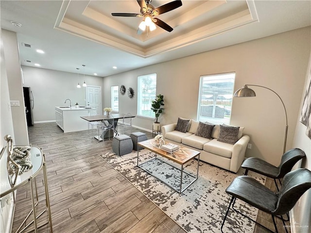 living room with ceiling fan, a raised ceiling, and sink