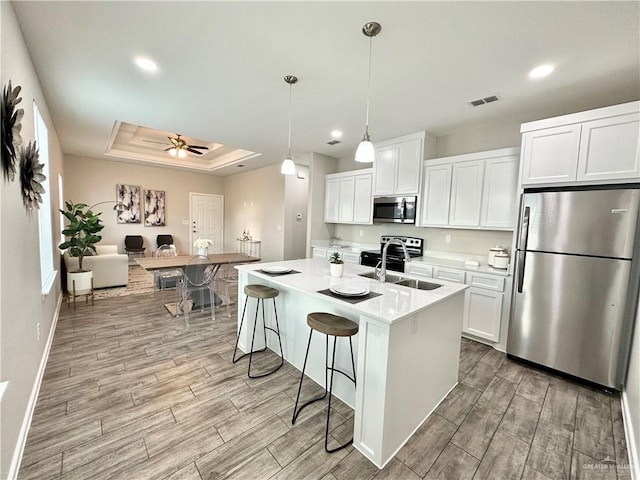 kitchen featuring a kitchen island with sink, hanging light fixtures, stainless steel appliances, and white cabinets