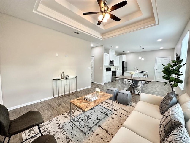 living room with ceiling fan, wood-type flooring, and a tray ceiling