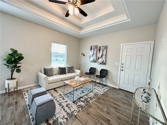 living room with dark hardwood / wood-style floors, ceiling fan, and a tray ceiling