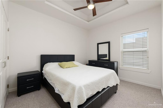 bedroom with light carpet, a raised ceiling, and ceiling fan