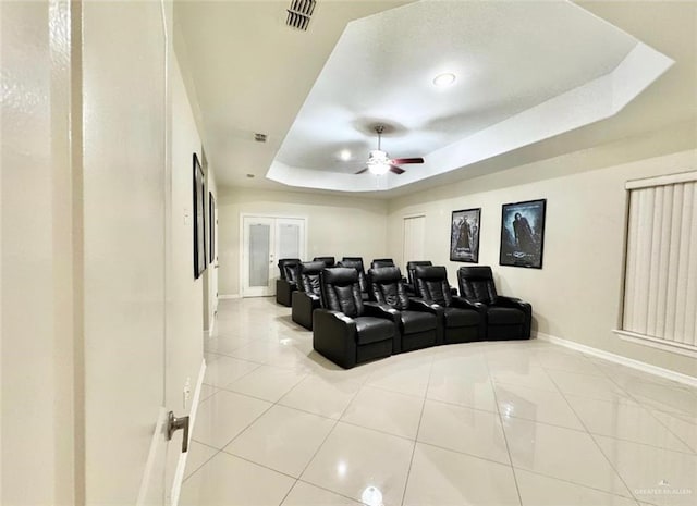 cinema room with light tile patterned floors, a tray ceiling, and ceiling fan