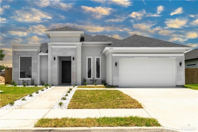 prairie-style home featuring driveway, a shingled roof, an attached garage, a front lawn, and stucco siding