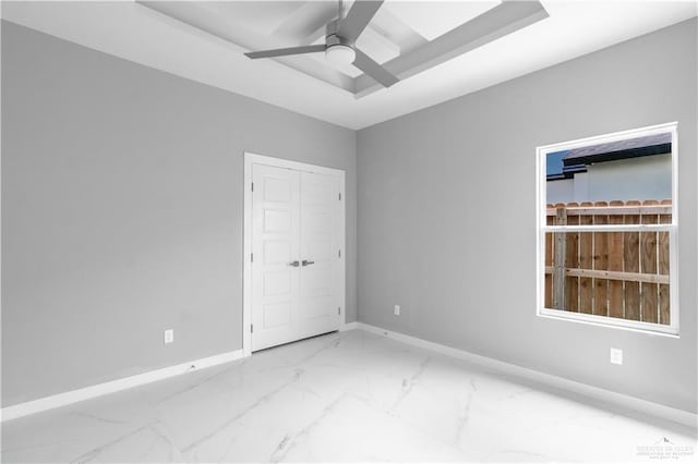 unfurnished room featuring marble finish floor, baseboards, a raised ceiling, and a ceiling fan