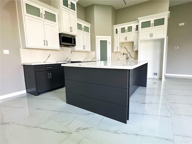 kitchen featuring marble finish floor, stainless steel microwave, backsplash, white cabinetry, and baseboards