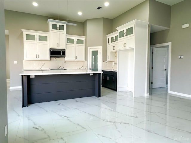 kitchen with marble finish floor, stainless steel microwave, white cabinets, and decorative backsplash