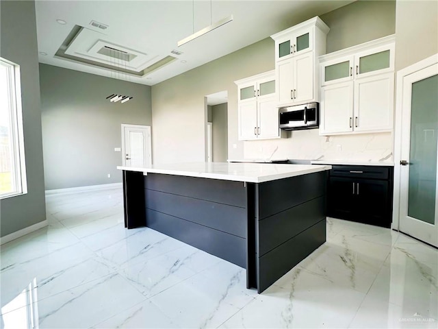 kitchen with white cabinets, marble finish floor, a large island, decorative backsplash, and stainless steel microwave