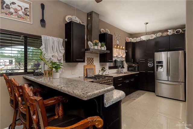 kitchen featuring wall chimney exhaust hood, hanging light fixtures, stainless steel appliances, backsplash, and a kitchen bar