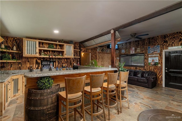 bar with ceiling fan and light stone countertops