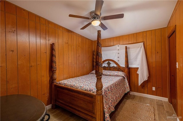 bedroom with ceiling fan, wooden walls, and light hardwood / wood-style floors