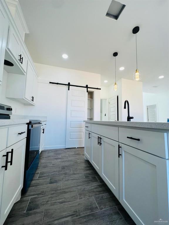 kitchen with sink, white cabinetry, decorative light fixtures, stainless steel range with electric cooktop, and a barn door