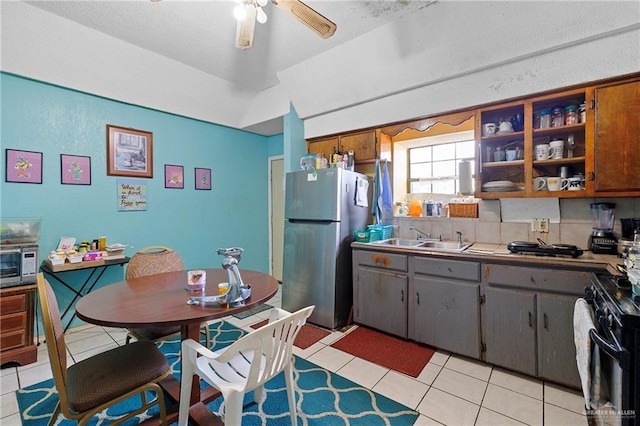 kitchen with stainless steel refrigerator, sink, black range with gas stovetop, light tile patterned floors, and ceiling fan