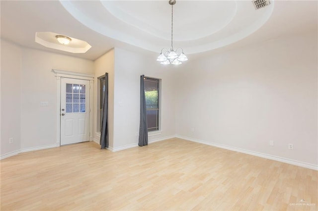 unfurnished room featuring a tray ceiling, light hardwood / wood-style flooring, and an inviting chandelier