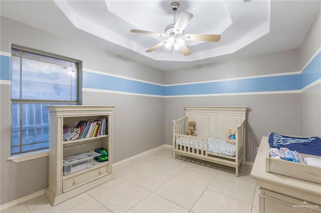 tiled bedroom with a raised ceiling, ceiling fan, and a crib