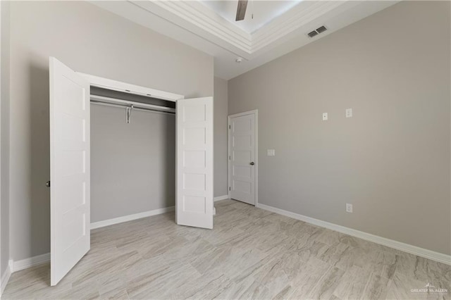 unfurnished bedroom with ceiling fan, crown molding, a tray ceiling, and a closet