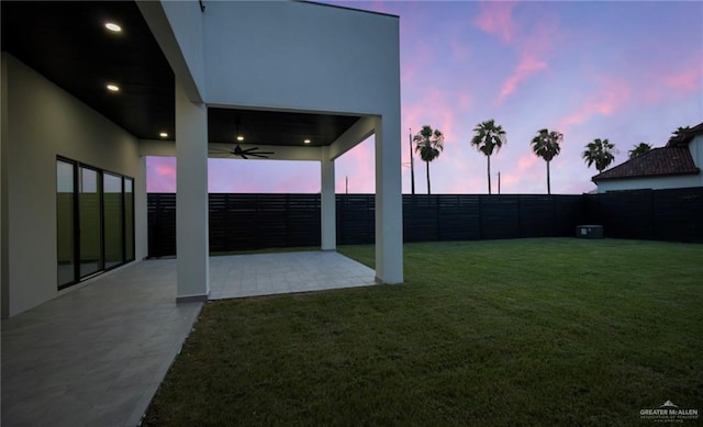 yard at dusk with a fenced backyard, ceiling fan, and a patio
